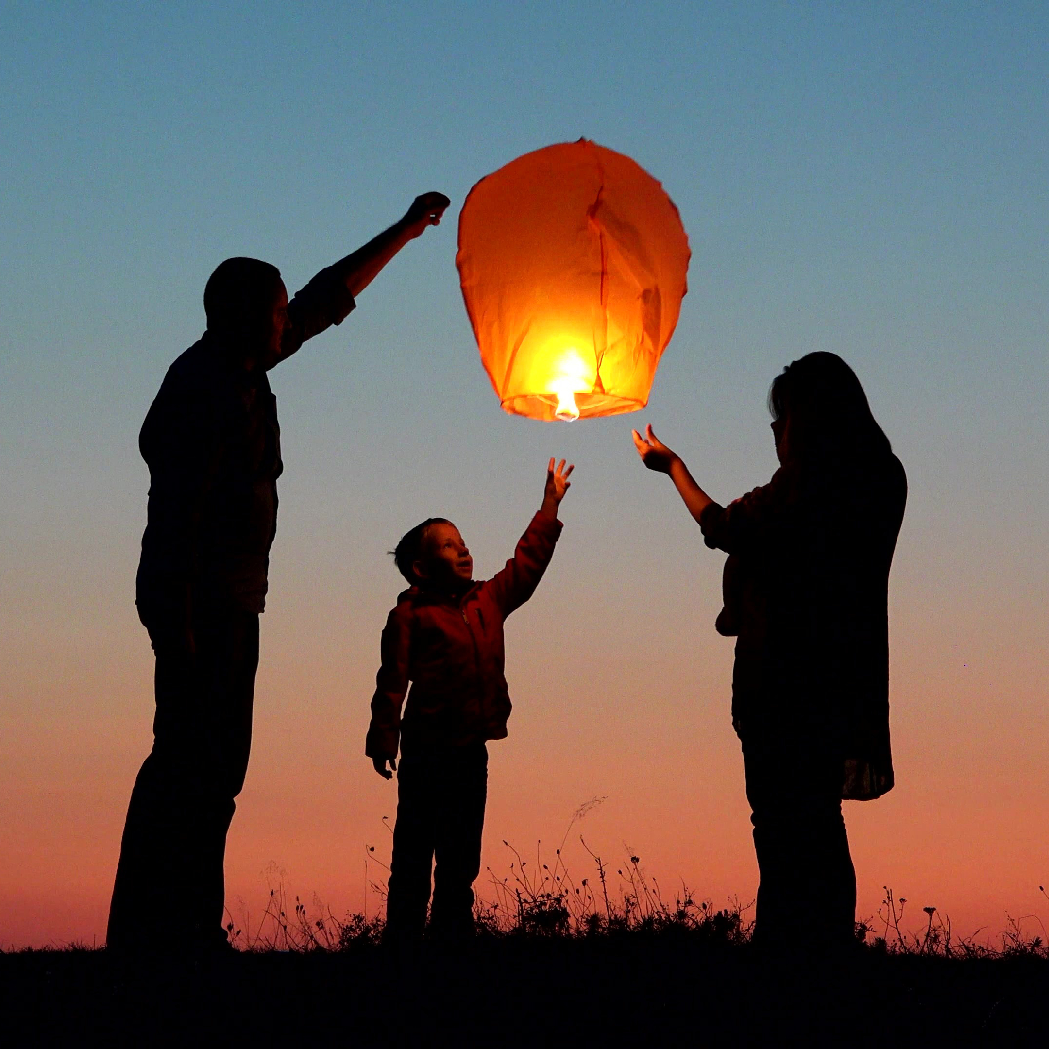 Parents, child and baby silhouette rising lightning sky lantern,